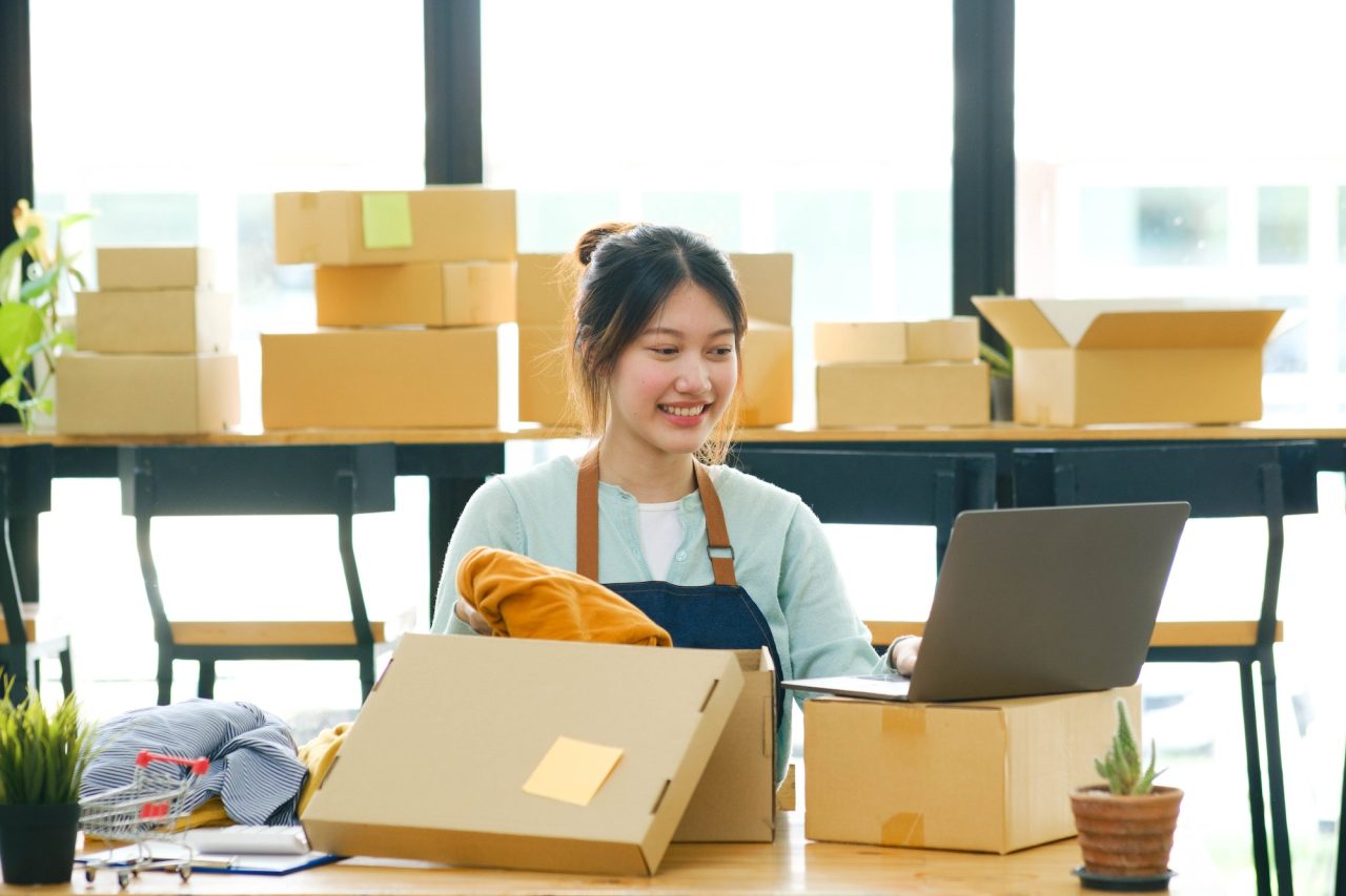Asian Female Clothes Shop Owner Folding A T Shirt And Packing In A Cardboard Parcel Box .jpg