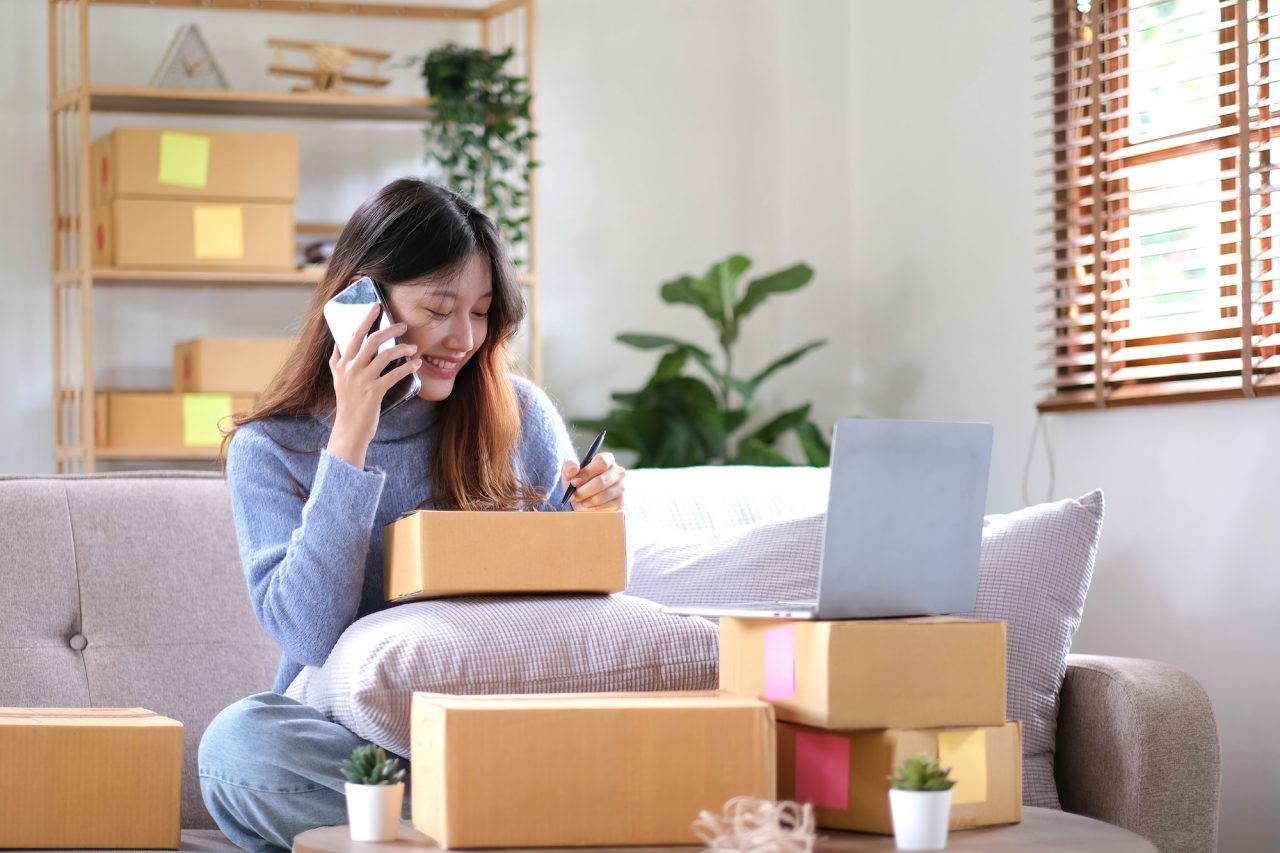 Portrait Young Asian Woman Using Laptop Computer For Work With Parcel Box On Sofa In Living Room.jpg