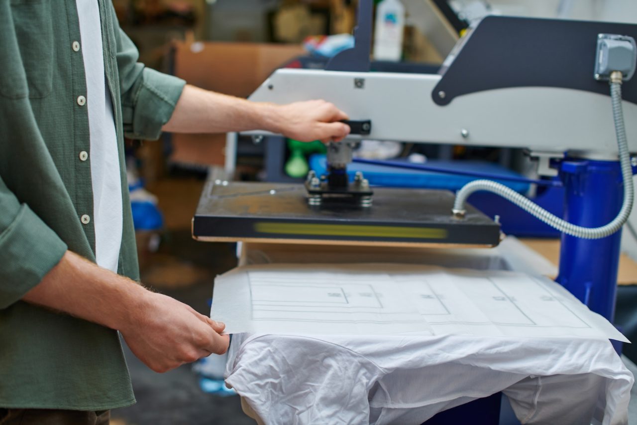 Cropped View Of Craftsman Holding Layer On T Shirt And Working With Screen Printing Machine 1.jpg